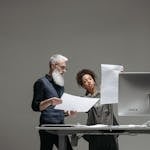 Two professionals collaborate on project plans at a computer workstation.